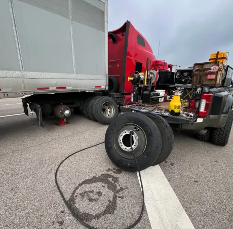 Breaux's Roadside service truck alongside a red semi tractor with a box trailer jacked up and the drive tire removed for replacement